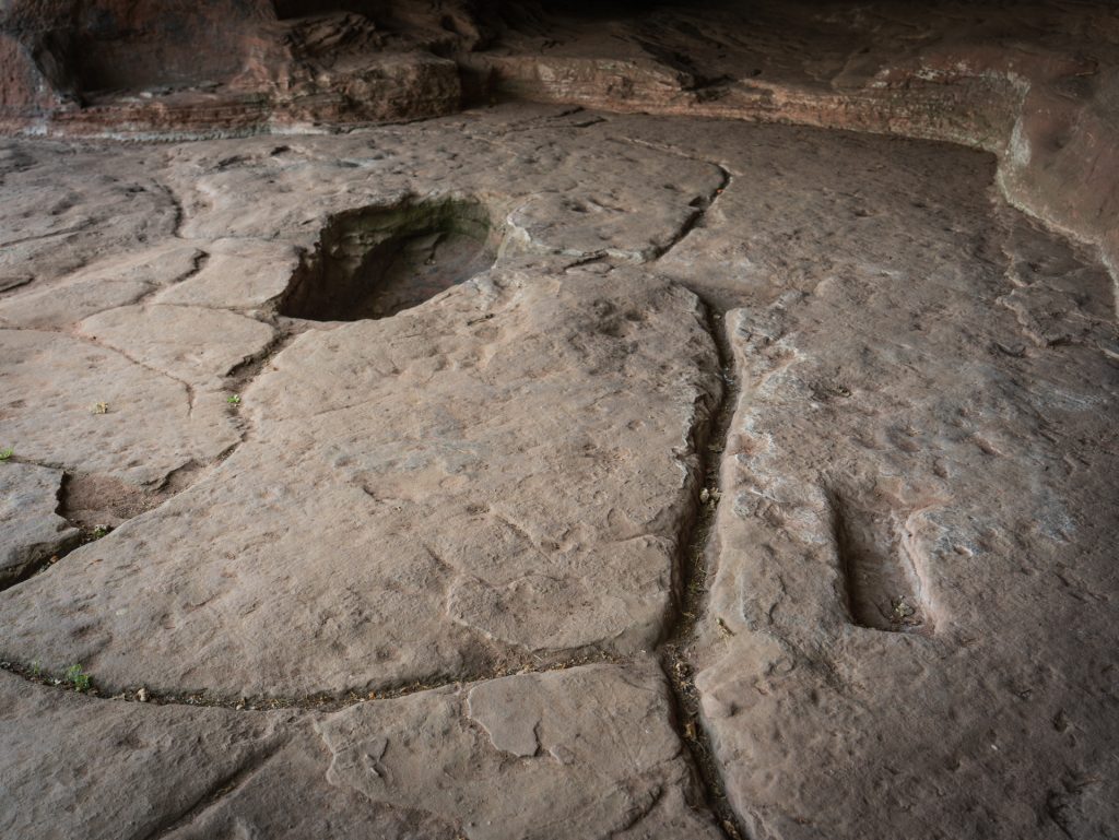 A rocky cave floor with visible surface textures and a noticeable circular depression, surrounded by eroded stone.