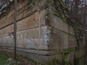 Close-up of a rugged sandstone cliff with visible layers, moss growth, and a nearby wooden pole.