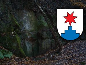 A rock wall covered in moss and foliage, featuring a faint carving of a star and an emblem with a red star above a blue shape.
